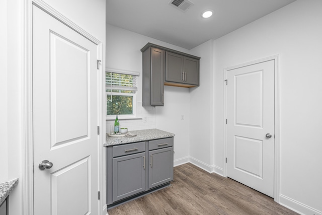 kitchen with dark wood-type flooring, light stone counters, and gray cabinetry