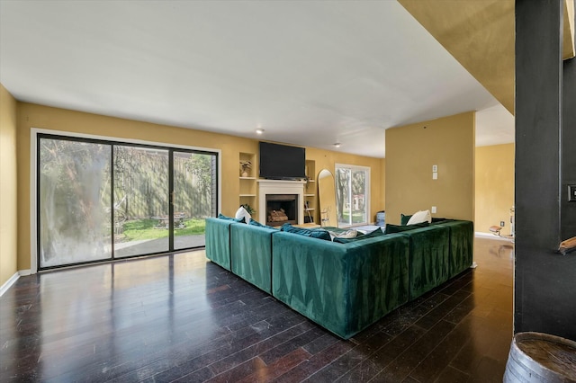 living room with built in shelves, baseboards, wood finished floors, and a fireplace