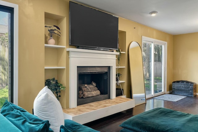 living area featuring built in shelves, wood finished floors, baseboards, and a fireplace with raised hearth