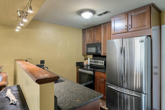 kitchen with visible vents, dark stone countertops, appliances with stainless steel finishes, a peninsula, and a sink