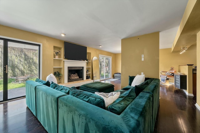 living room featuring dark wood-style floors, built in features, and a fireplace with raised hearth