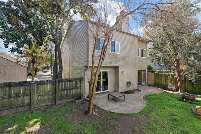 back of house with a lawn, a fenced backyard, a chimney, and a patio area