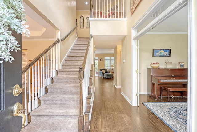entryway featuring stairs, wood finished floors, a towering ceiling, baseboards, and ornamental molding