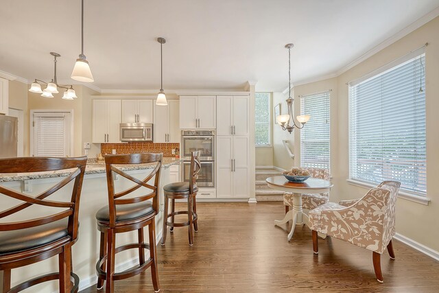 kitchen featuring appliances with stainless steel finishes, a chandelier, wood finished floors, crown molding, and plenty of natural light