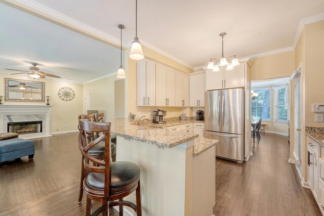 kitchen with freestanding refrigerator, a peninsula, dark wood finished floors, baseboards, and ornamental molding