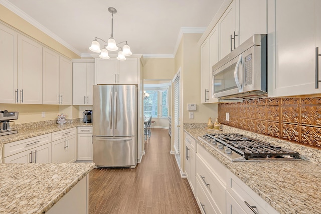 kitchen featuring stainless steel appliances, baseboards, crown molding, light wood-style floors, and a chandelier