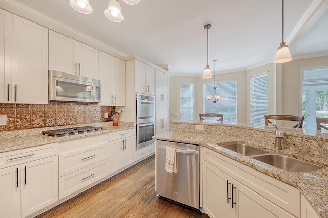 kitchen featuring appliances with stainless steel finishes, a sink, crown molding, wood finished floors, and decorative backsplash