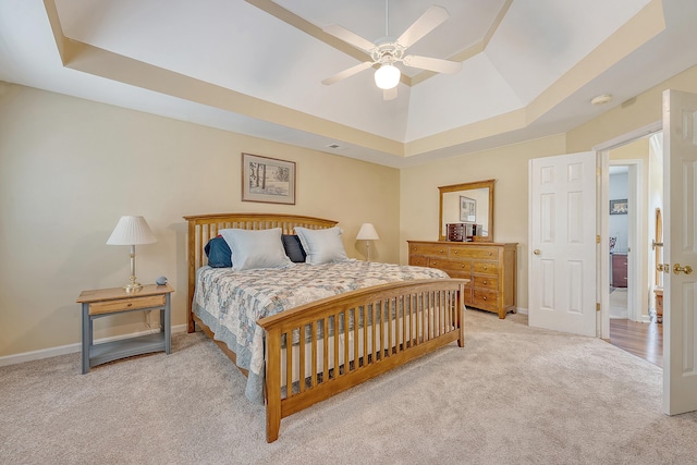 carpeted bedroom featuring a tray ceiling, baseboards, and ceiling fan