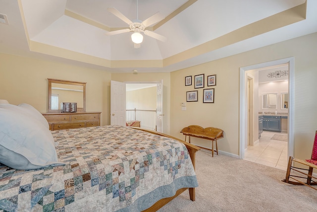 bedroom with a raised ceiling, light carpet, baseboards, a ceiling fan, and ensuite bathroom