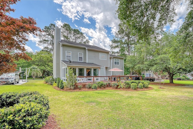 rear view of property featuring a chimney, a lawn, and a wooden deck