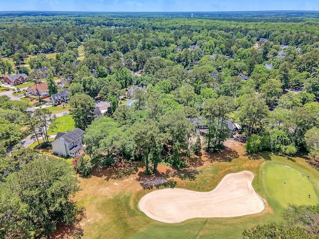 aerial view of property and surrounding area featuring a golf course and a forest