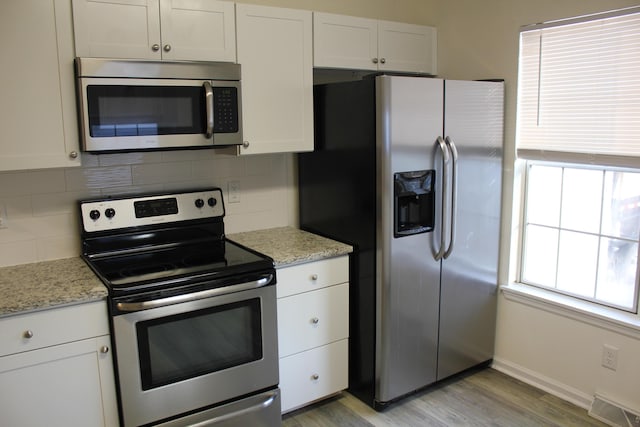 kitchen featuring white cabinetry, stainless steel appliances, tasteful backsplash, light stone countertops, and light wood-type flooring