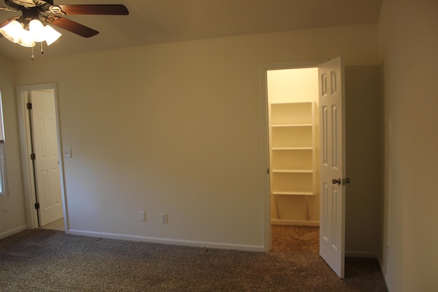 unfurnished bedroom featuring ceiling fan, a spacious closet, and dark carpet