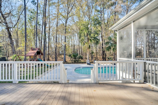 view of swimming pool with a playground, a wooden deck, and a sunroom