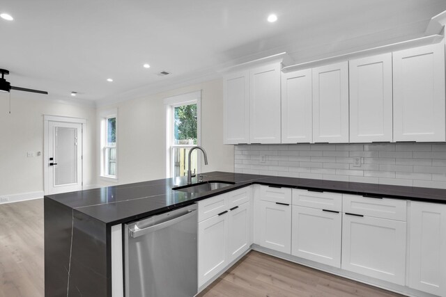 kitchen featuring stainless steel dishwasher, a sink, light wood-type flooring, tasteful backsplash, and dark countertops