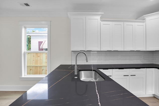kitchen with a sink, tasteful backsplash, wood finished floors, and white cabinetry