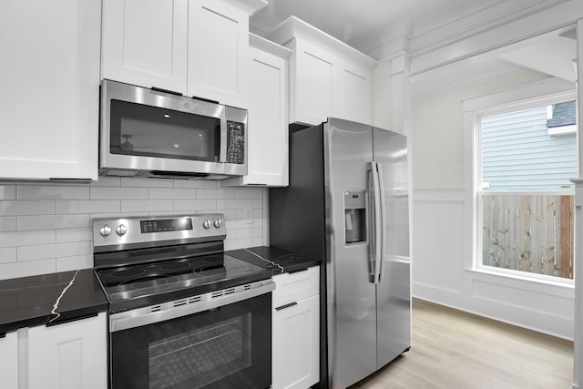 kitchen with stainless steel appliances, white cabinetry, light wood-type flooring, tasteful backsplash, and a wainscoted wall
