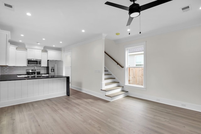kitchen featuring stainless steel appliances, crown molding, a sink, dark countertops, and light wood-type flooring