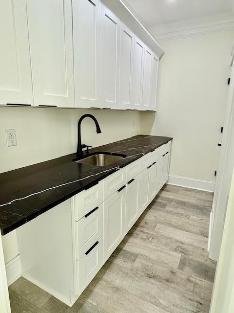 kitchen with a sink, dark countertops, white cabinetry, and ornamental molding