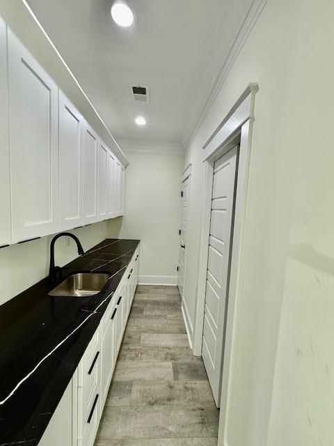 kitchen featuring a sink, dark countertops, crown molding, light wood-type flooring, and white cabinets