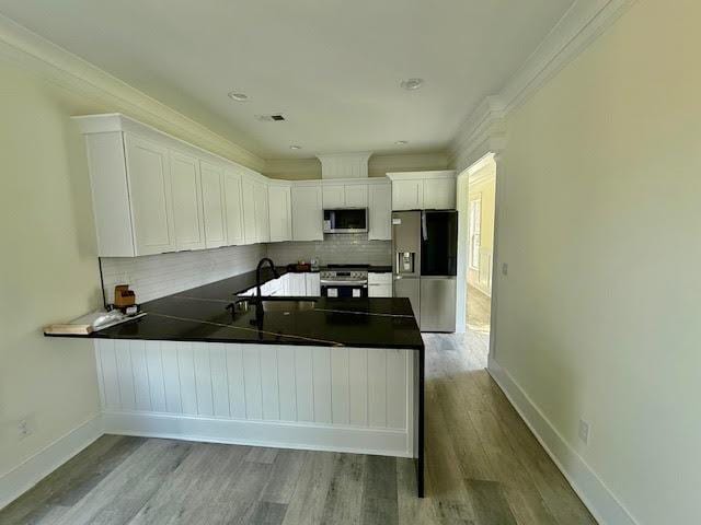 kitchen featuring stainless steel appliances, dark countertops, a peninsula, tasteful backsplash, and crown molding