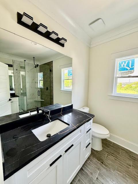bathroom with a stall shower, toilet, vanity, baseboards, and wood finish floors