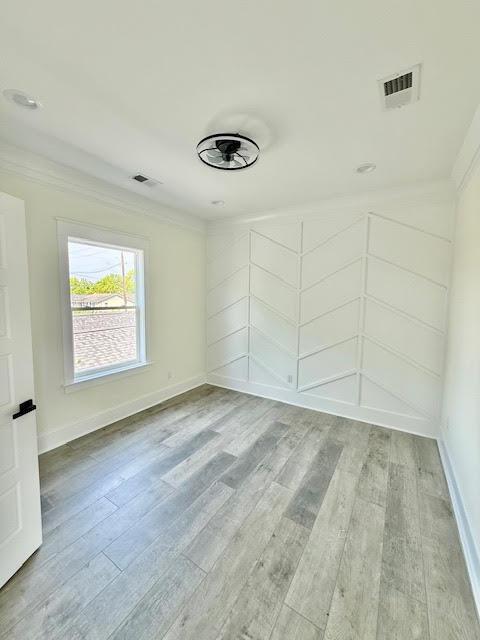 empty room with crown molding, light wood-style flooring, and baseboards