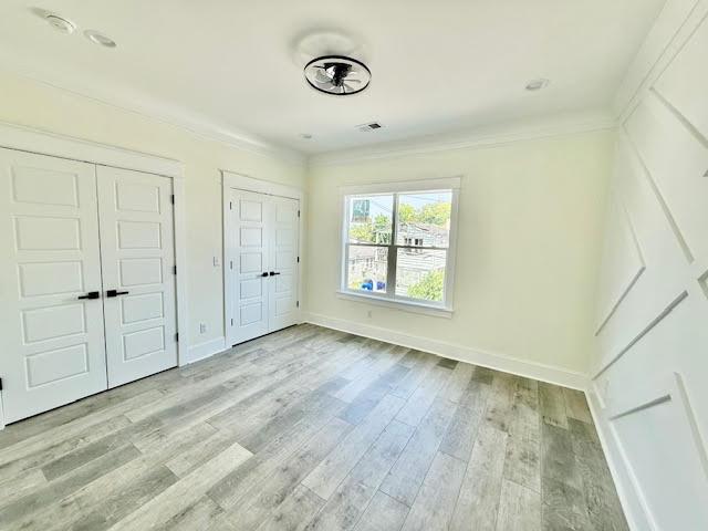 unfurnished bedroom featuring multiple closets, wood finished floors, baseboards, and ornamental molding