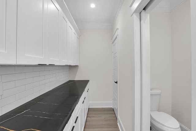 kitchen featuring white cabinetry, dark countertops, ornamental molding, backsplash, and light wood-type flooring