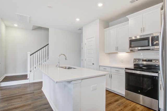 kitchen featuring visible vents, appliances with stainless steel finishes, wood finished floors, a sink, and backsplash