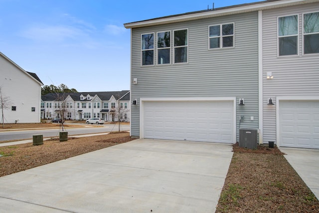 view of side of home with a residential view, driveway, an attached garage, and central AC unit