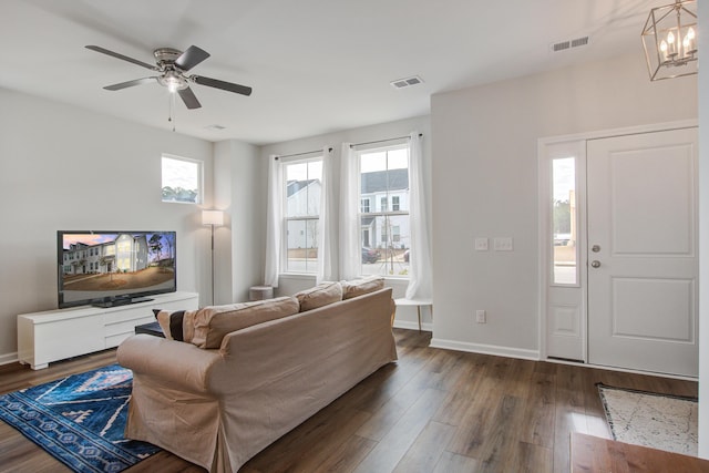 living room featuring dark wood-style flooring, visible vents, baseboards, and ceiling fan with notable chandelier