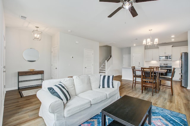 living room with light wood-style floors, visible vents, stairway, and ceiling fan with notable chandelier