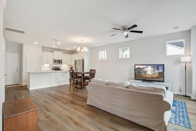 living room with baseboards, visible vents, light wood finished floors, and ceiling fan with notable chandelier