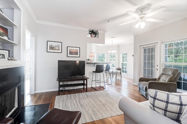 living area with a fireplace with flush hearth, wood finished floors, a wealth of natural light, and ornamental molding