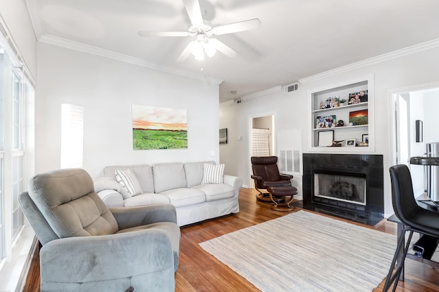 living room with visible vents, ornamental molding, wood finished floors, a tile fireplace, and a ceiling fan