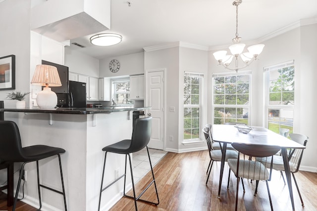 kitchen featuring fridge, a breakfast bar, an inviting chandelier, light wood finished floors, and a peninsula