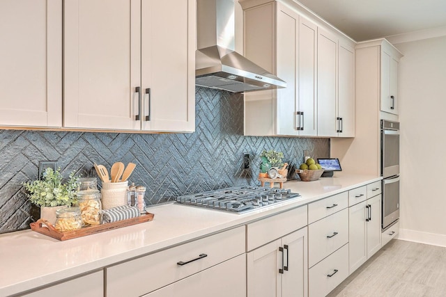 kitchen featuring decorative backsplash, wall chimney exhaust hood, stainless steel appliances, light wood-type flooring, and white cabinets