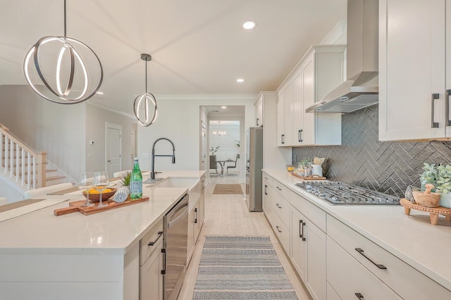 kitchen with appliances with stainless steel finishes, wall chimney exhaust hood, a center island with sink, and hanging light fixtures