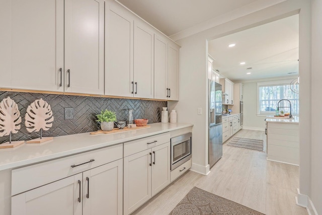 kitchen featuring light wood-type flooring, backsplash, stainless steel appliances, white cabinets, and crown molding