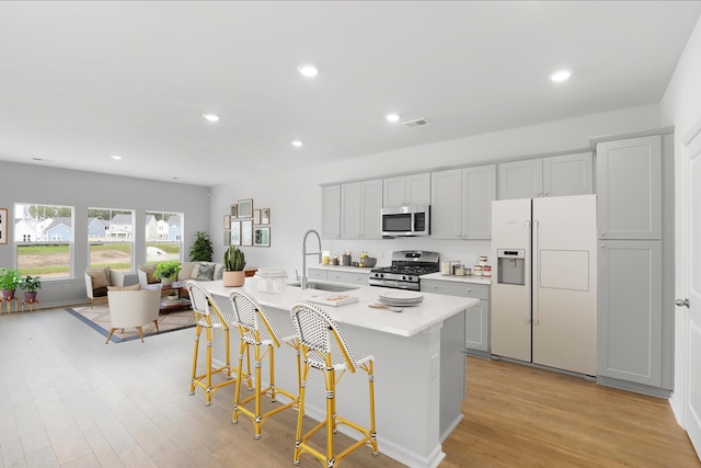 kitchen featuring sink, a center island with sink, appliances with stainless steel finishes, a kitchen breakfast bar, and light hardwood / wood-style floors