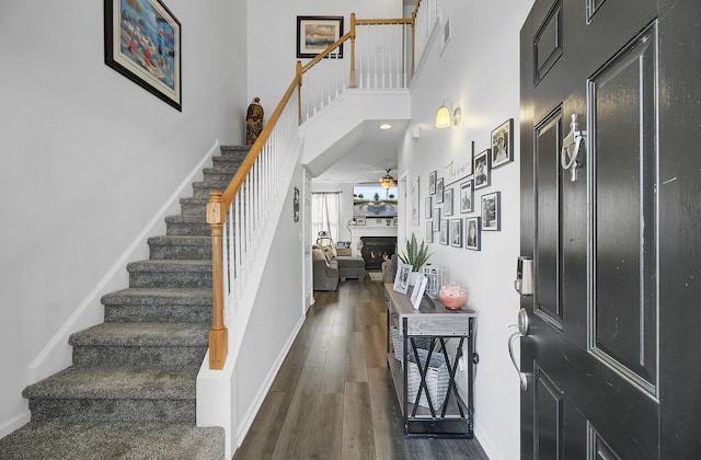 foyer entrance featuring baseboards, stairs, a lit fireplace, a towering ceiling, and wood finished floors