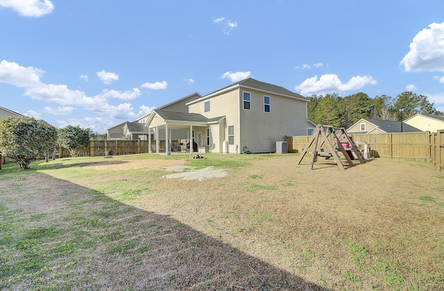 rear view of property featuring a playground, a lawn, and a fenced backyard