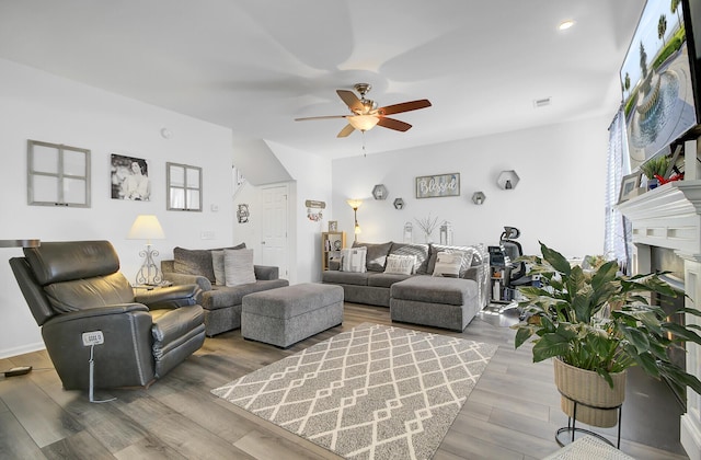 living room with a fireplace, wood finished floors, visible vents, and ceiling fan