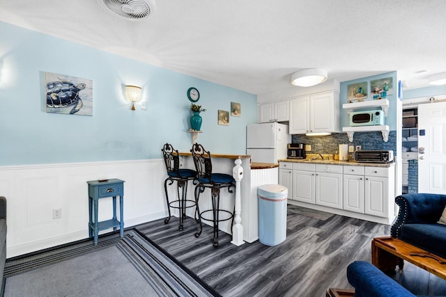 kitchen with a wainscoted wall, a toaster, visible vents, white cabinets, and white appliances