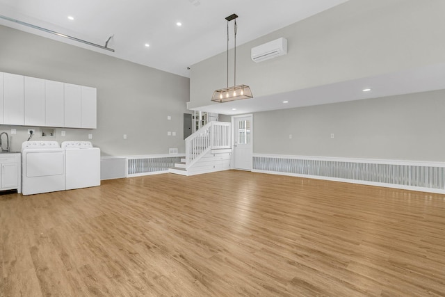 unfurnished living room featuring a wall mounted AC, washer and clothes dryer, and light hardwood / wood-style floors