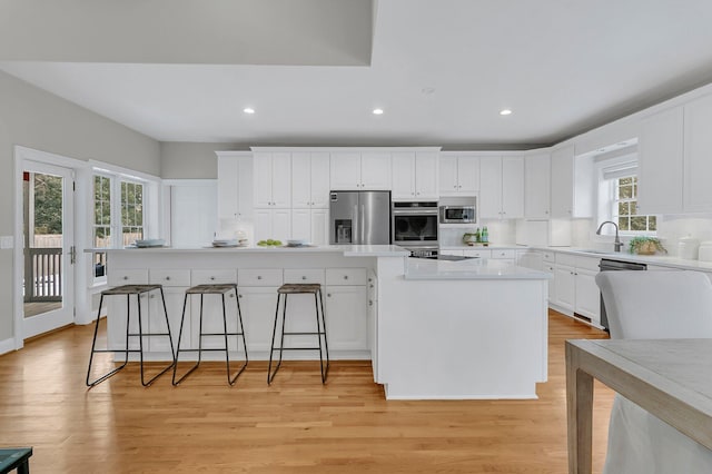 kitchen with stainless steel appliances, a center island, white cabinets, and light hardwood / wood-style flooring