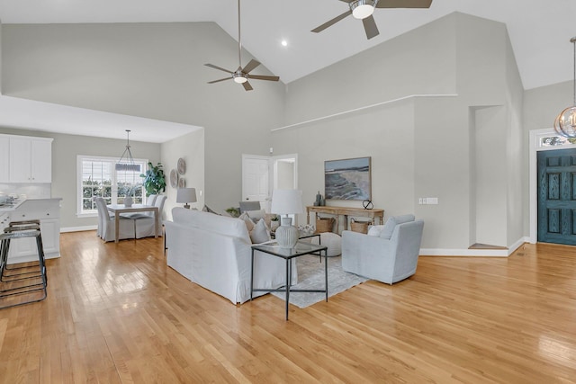 living room featuring ceiling fan with notable chandelier, high vaulted ceiling, and light hardwood / wood-style flooring