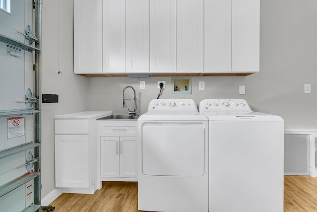 laundry area featuring cabinets, separate washer and dryer, sink, and light hardwood / wood-style flooring