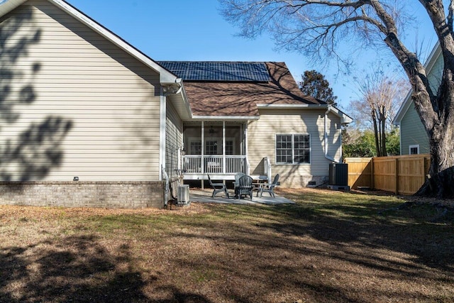 rear view of house with cooling unit, a yard, a patio, a sunroom, and solar panels